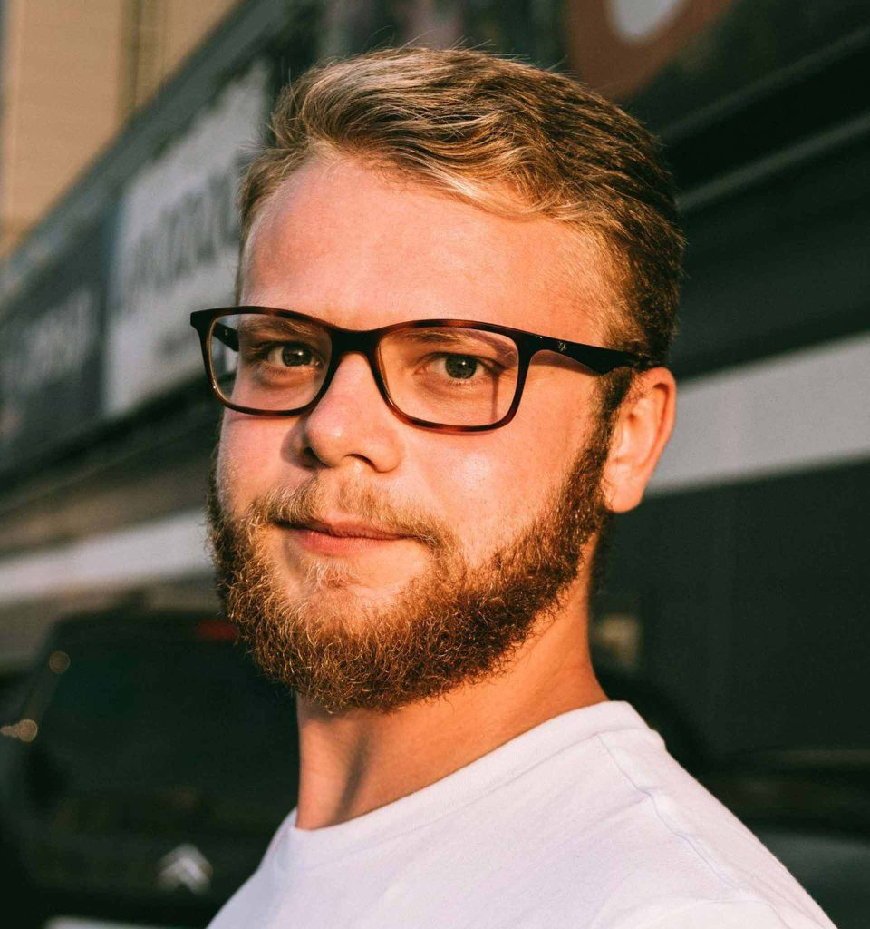 A man wearing a white T-shirt and rectangle tortoiseshell glasses