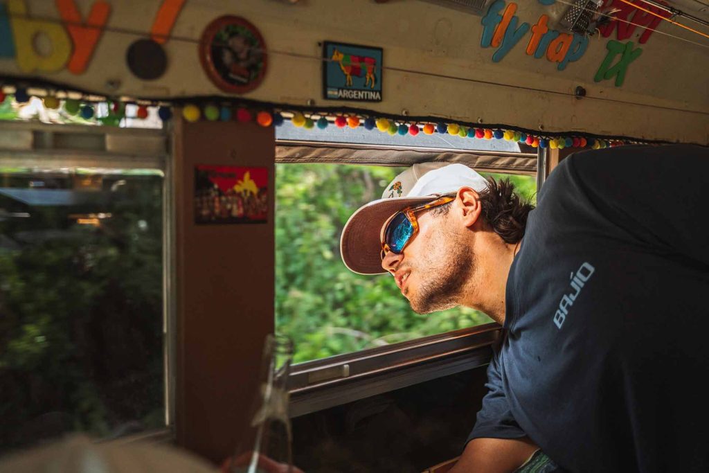 Traveling man wearing Bajío sunglasses as he leans out a bus window to enjoy the view