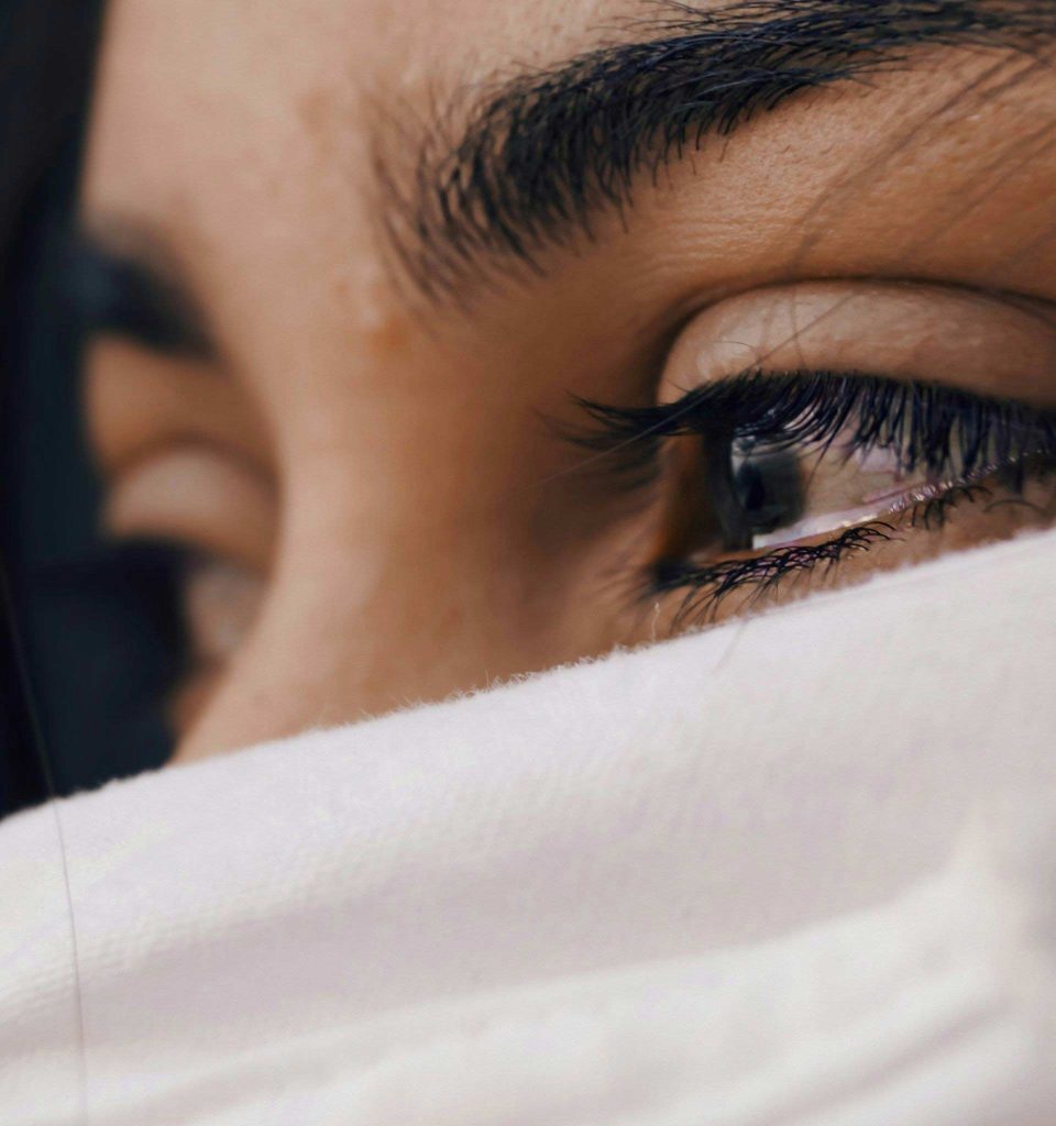 A woman with brown watery eyes holding a white scarf across her face
