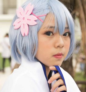 A young woman wearing a blue-grey wig, light makeup, and big, deep-blue cosplay contact lenses