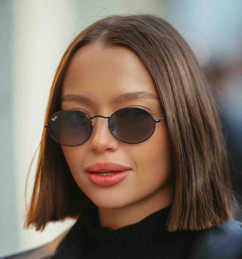 Stylish woman, wearing oval sunglasses and a black mock turtleneck, posing against a neutral background