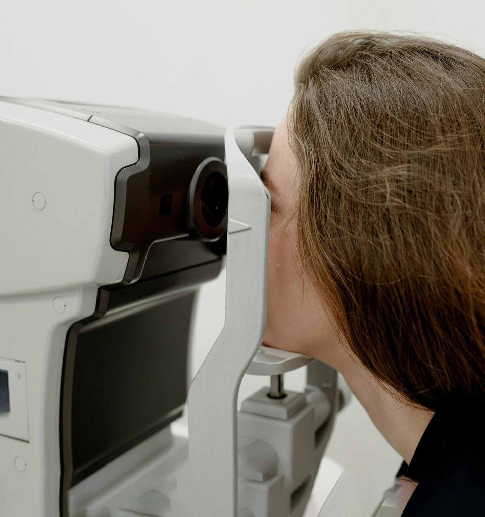 A woman with her face resting in front of a piece of specialized equipment used for eye exams