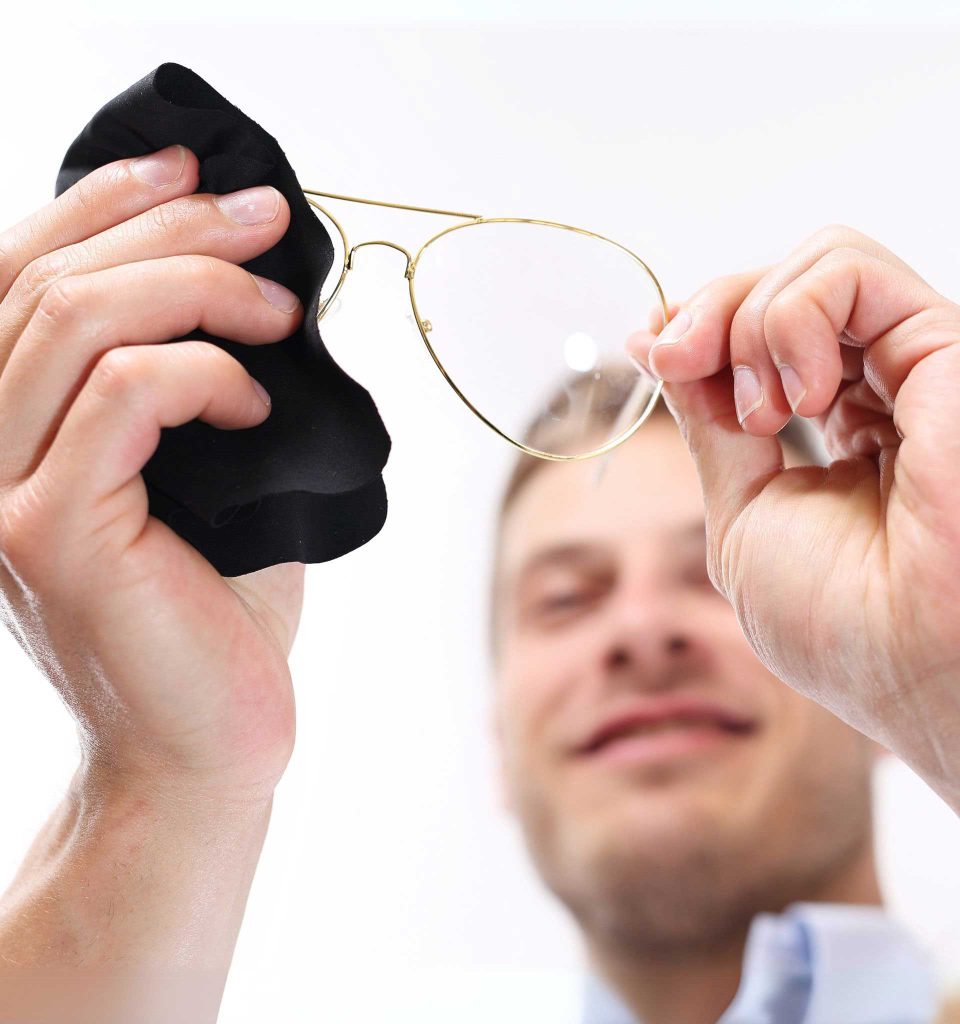 A man cleaning an eyeglass lens with a microfiber cloth, ensuring clear lenses and proper eyewear maintenance