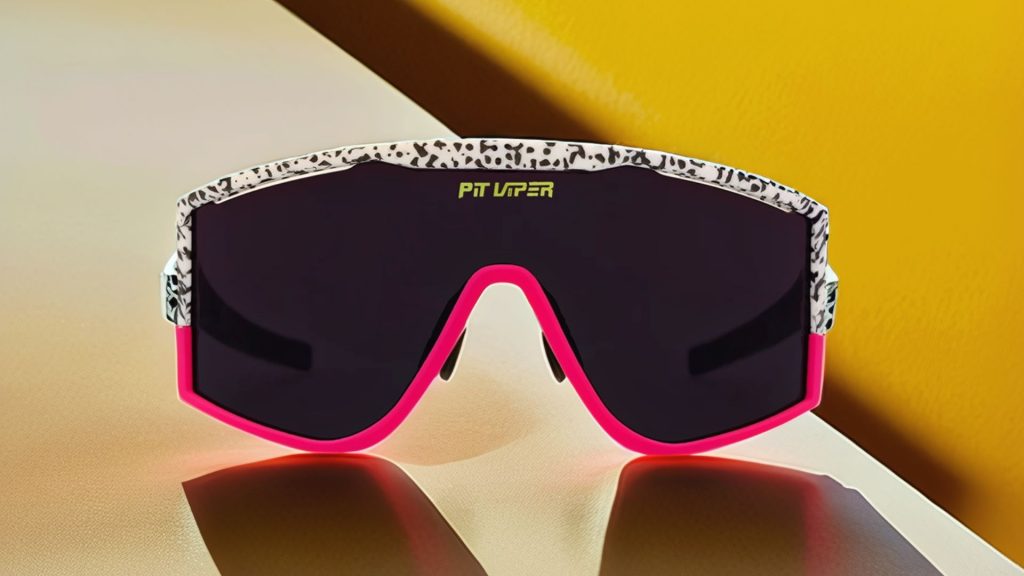 A pair of large-rimmed gray lensed Pit Viper shades with a black and white upper rim and neon pink bottom rim