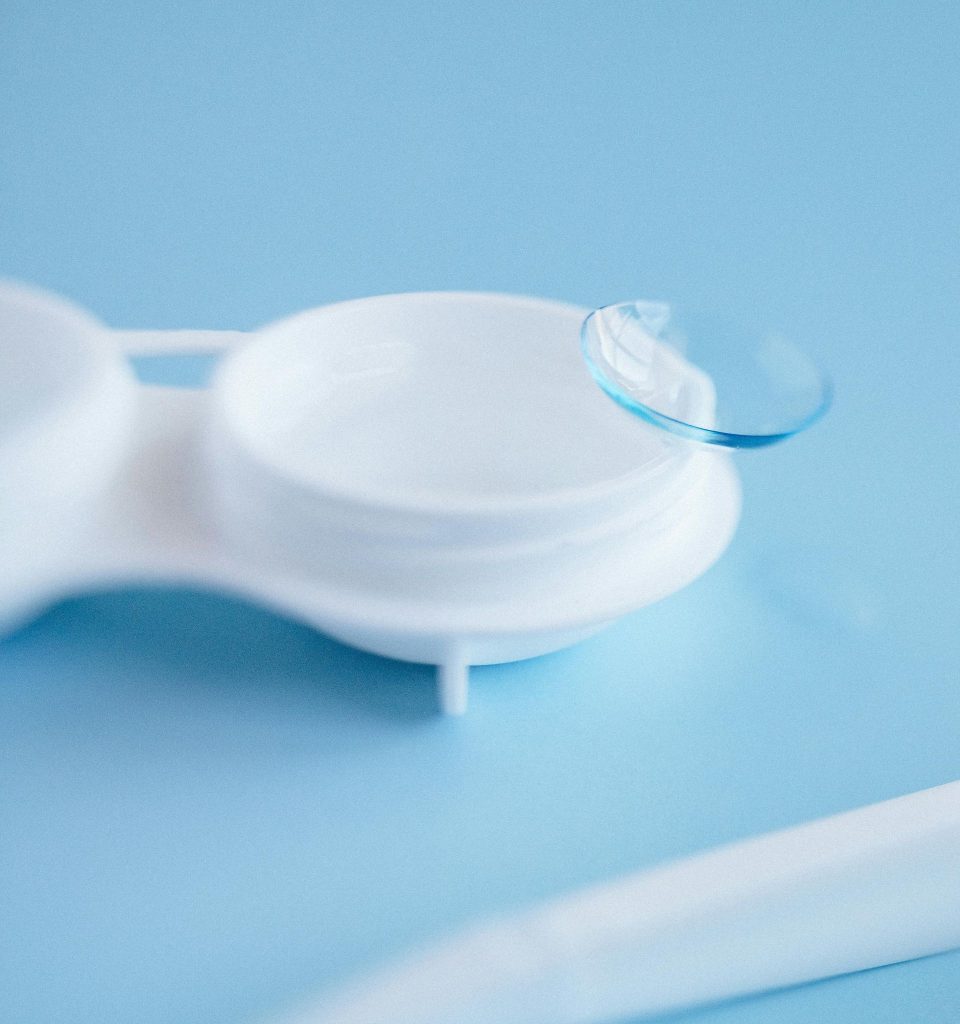 A contact lens sits on the edge of a case with applicators nearby