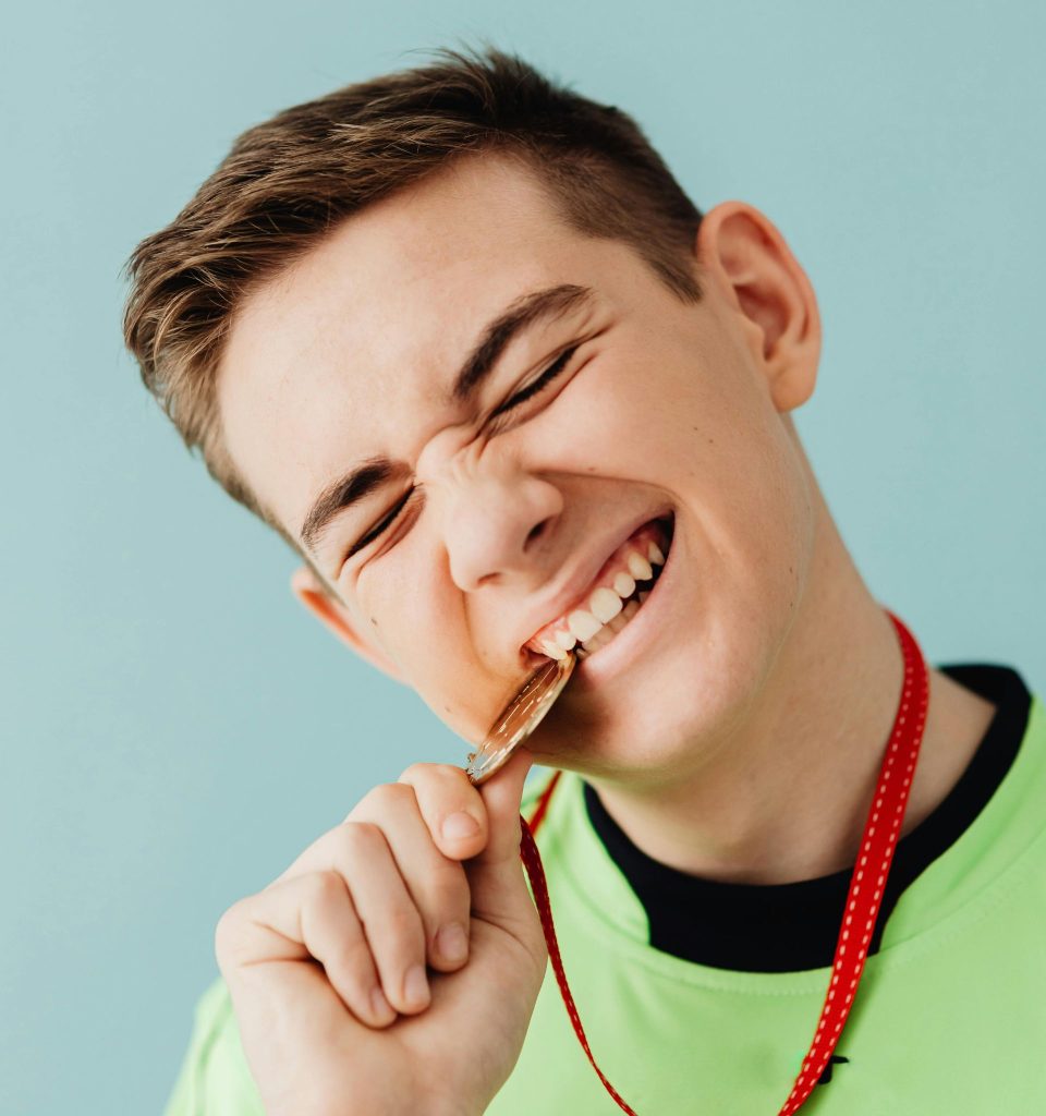 A boy biting a gold medal hung around his neck