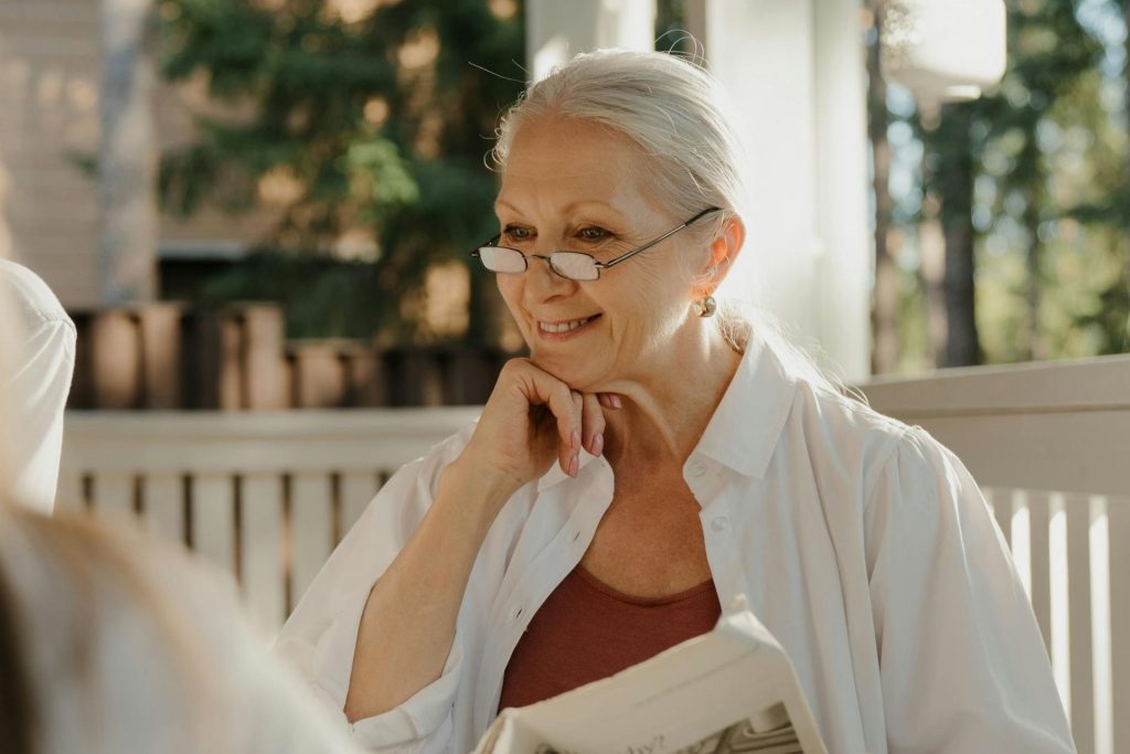 Woman on her porch wearing reading glasses to see the newspaper