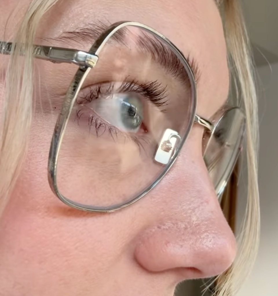 A woman's long eyelashes are touching the lenses of her glasses
