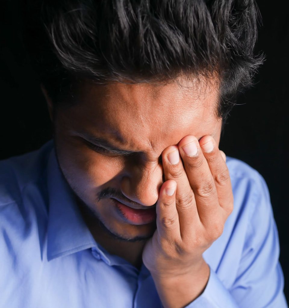 A man visibly in pain, holding his left hand over his left eye
