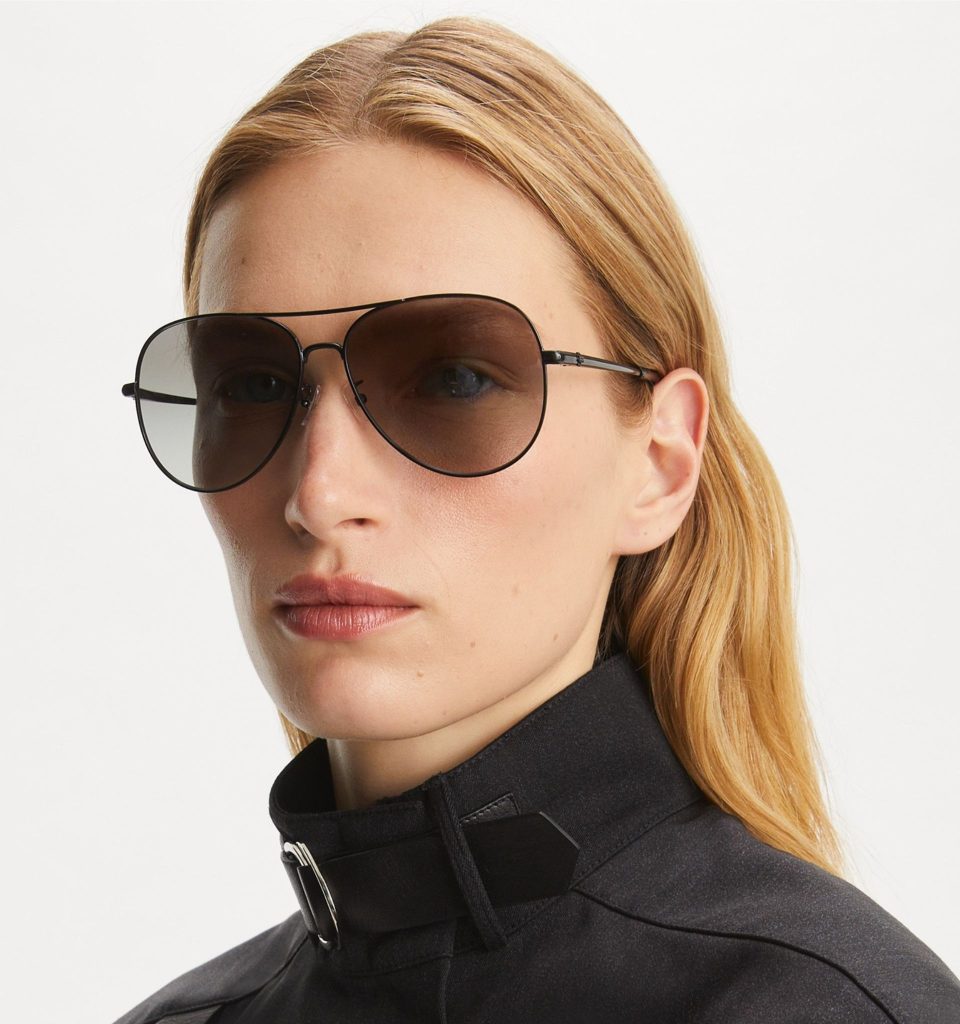 A model wearing Tory Burch Eleanor Pilot sunglasses with lightweight black metal frames, a polished metal bridge, and dark tinted lenses