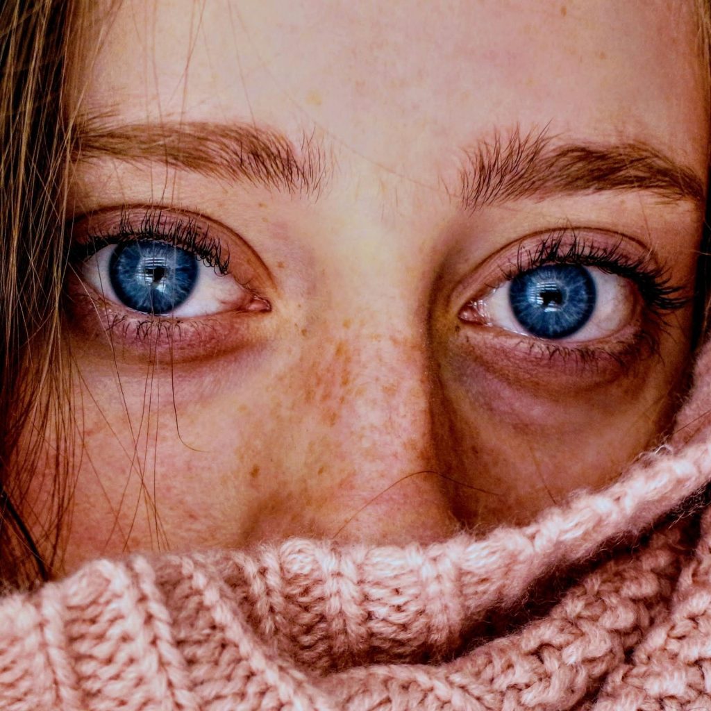 A woman’s blue eyes peek through a pink sweater