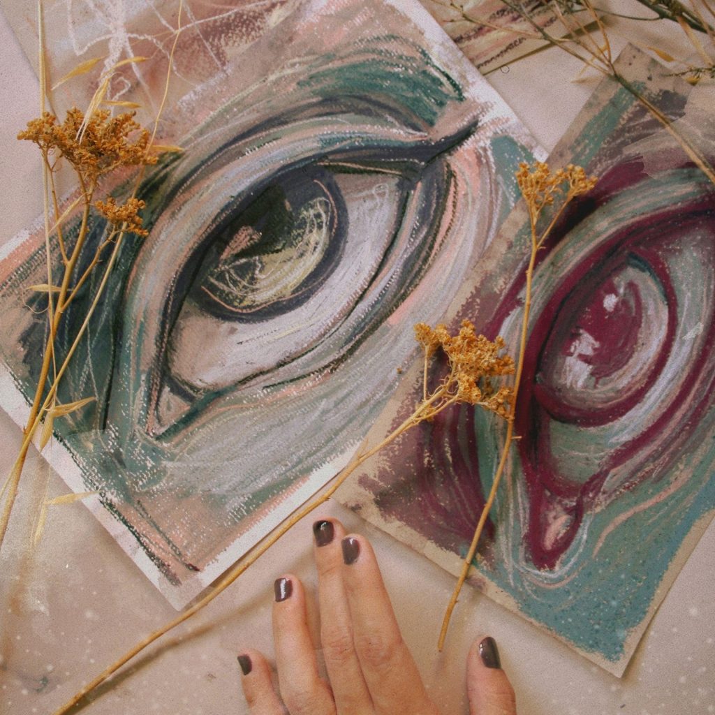 Red, green, and yellow chalk sketches of eyes, surrounded by dried flowers