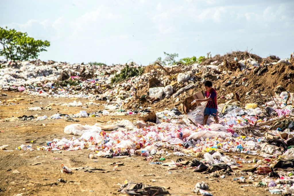 A boy walking through a landfill full of plastic and waste