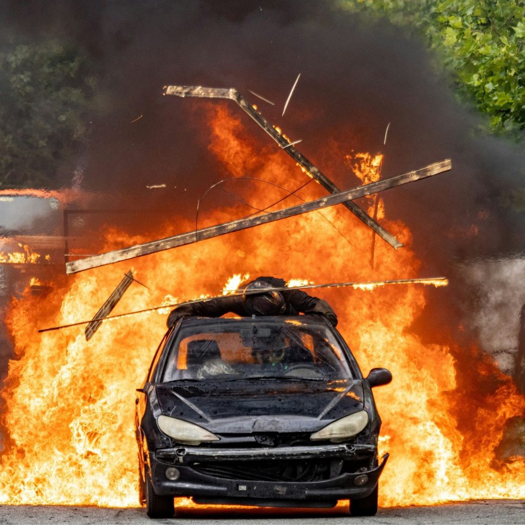 Black stunt car driving through a flaming explosion
