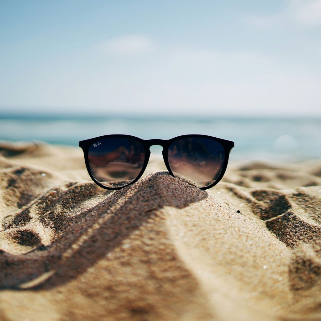 Ray-ban sunglasses sit on a sandy beach while the sun is high