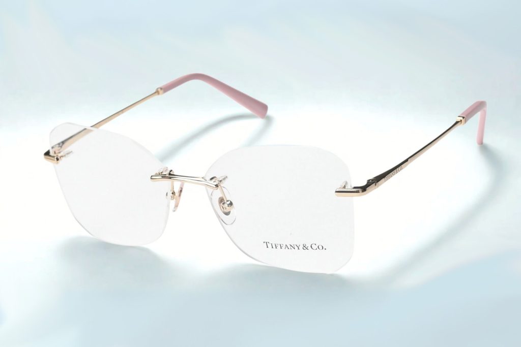 Rimless glasses featuring square lenses with rounded edges, thin gold arms, and pink rubberized temple tips