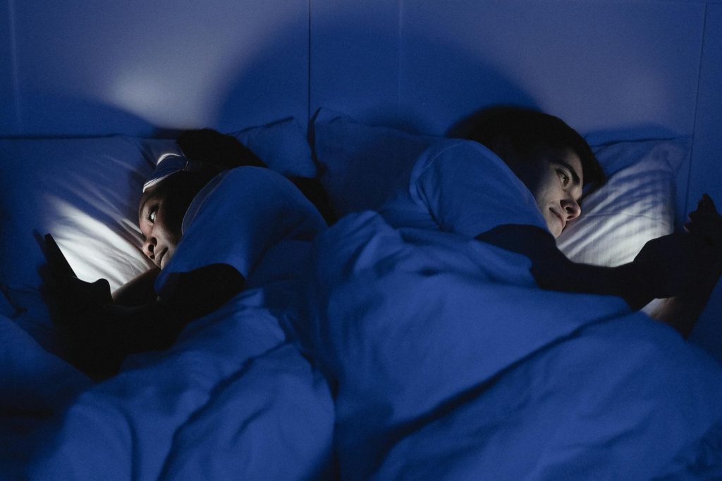 A couple reading from smartphones while in bed