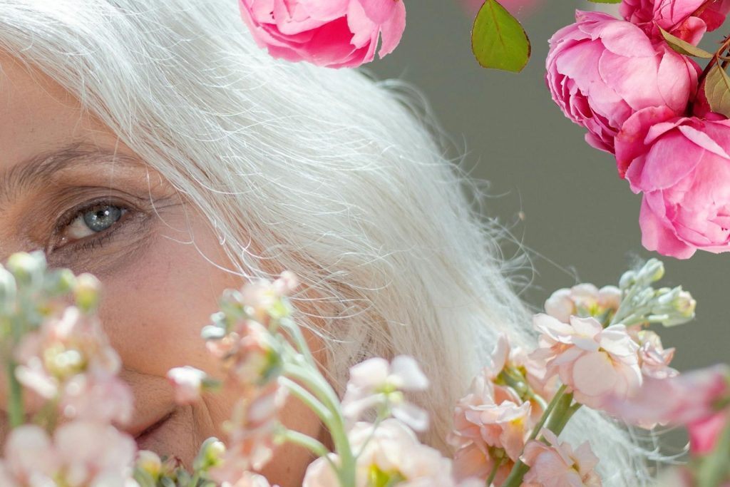 White-haired woman with flowers in the foreground and background