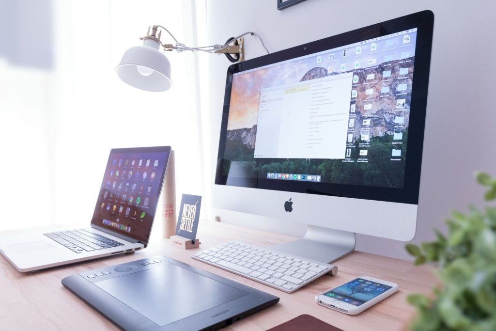 Devices, including a computer, laptop, and phone, placed on a desk