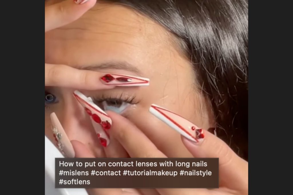 Woman putting in a contact lens with long acrylic nails