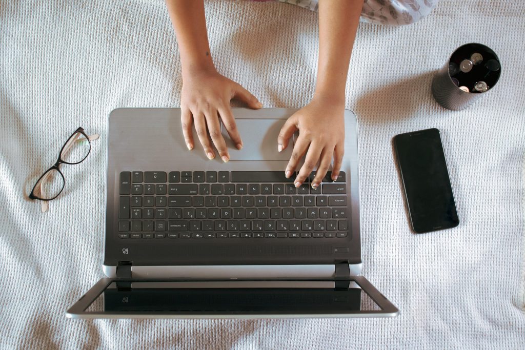 A person typing on a laptop, with glasses and a smartphone nearby