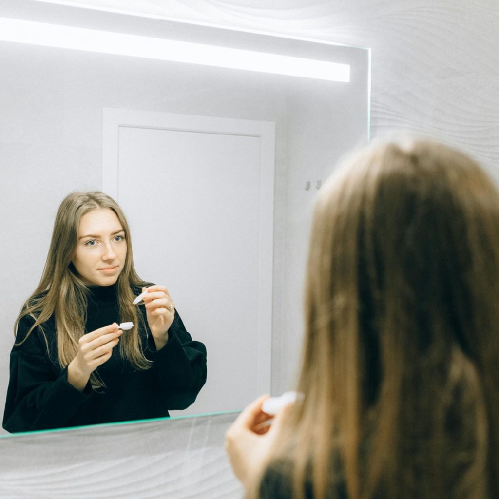 Woman putting in contact lenses in front of a mirror