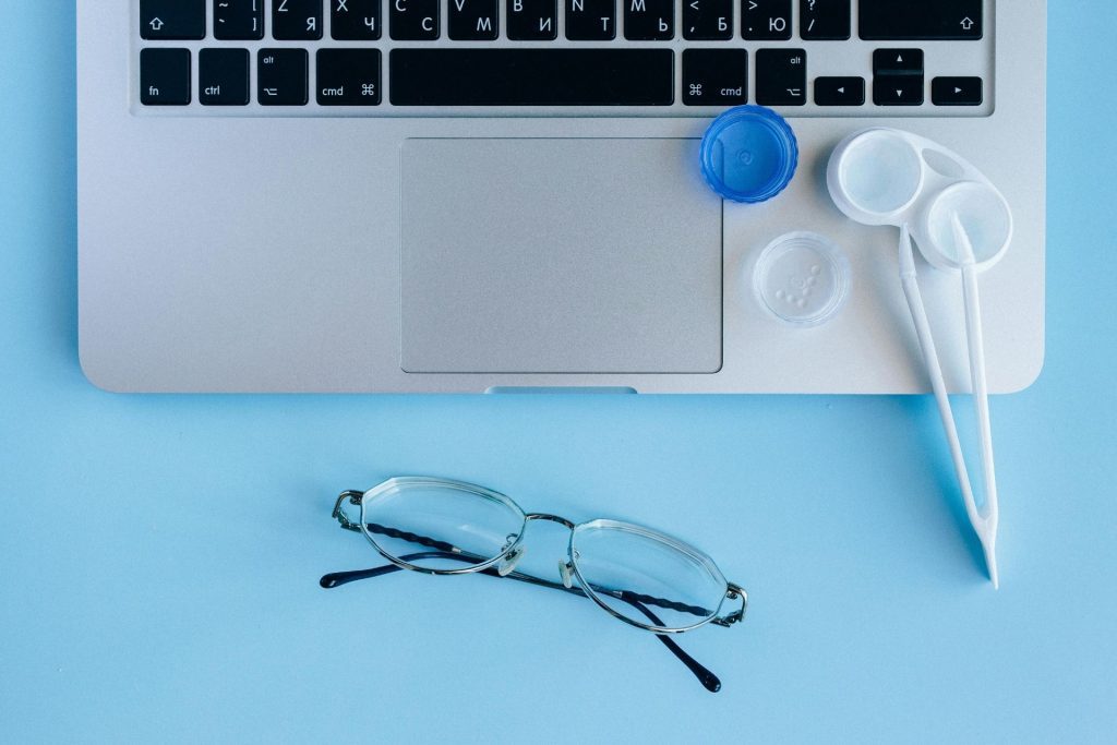 Laptop and eyeglasses on top of a blue table; contact lens kit placed above the laptop