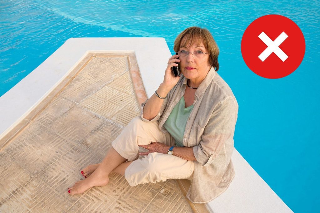 Woman sitting by a pool wearing summer clothes and rimless glasses