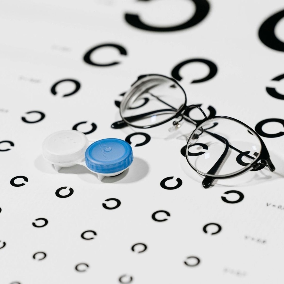 A contact lens case and pair of eyeglasses on top of an eye chart