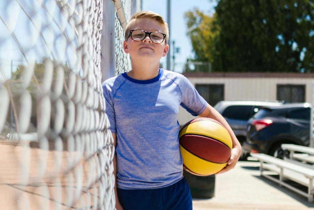 Boy holding a basketball, leaning against a fence