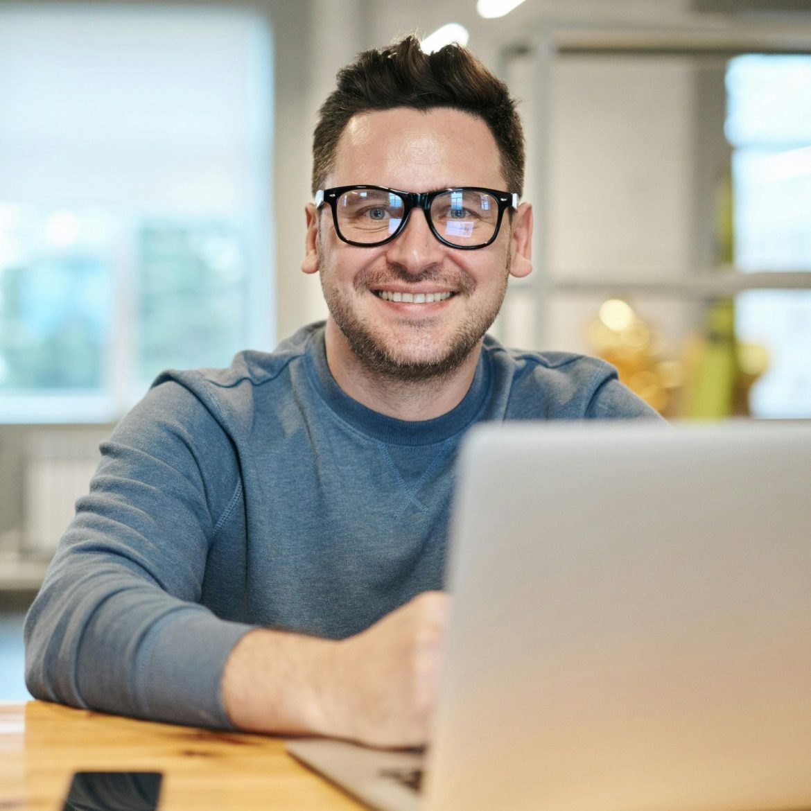 Man sitting in front of a laptop, wearing black glasses