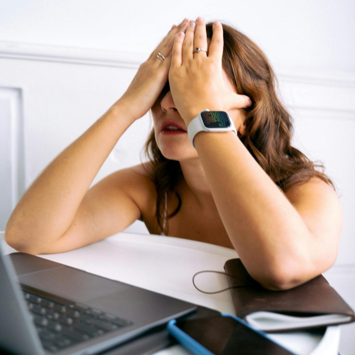 Woman covers her eyes in frustration while in front of her laptop