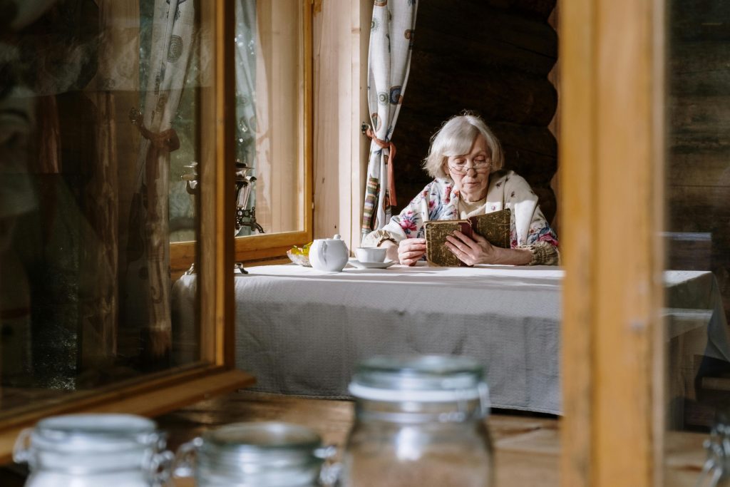 Woman sitting at a table with a teapot, reading a book