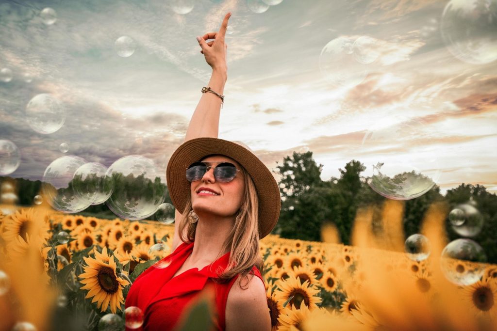 A woman wearing sunglasses looks up while in the middle of a sunflower field