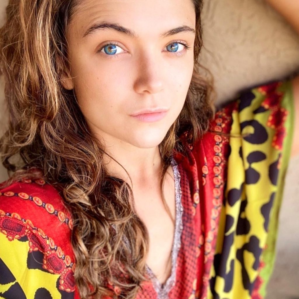 A woman with hazel eyes, wearing a red and yellow outfit