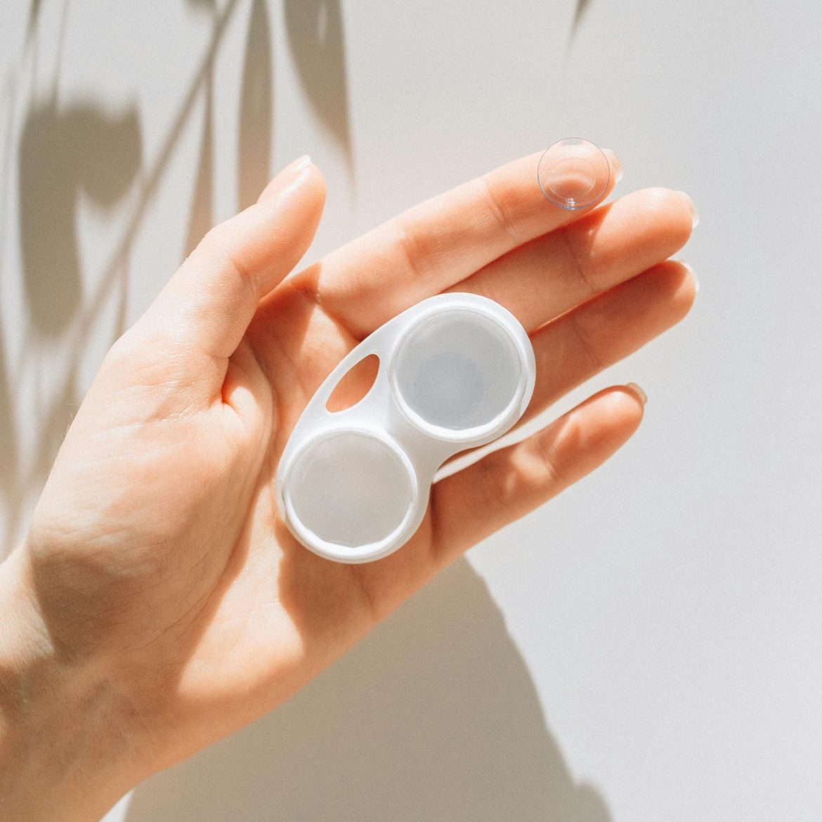 A hand holding a lens case and a contact lens