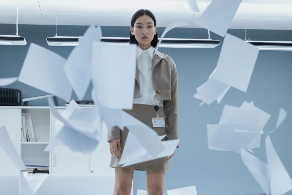 A woman stands on top of a table; documents are up in the air