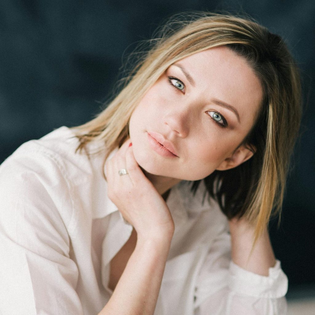Woman with gray eyes, wearing a buttoned-down white shirt and black pants