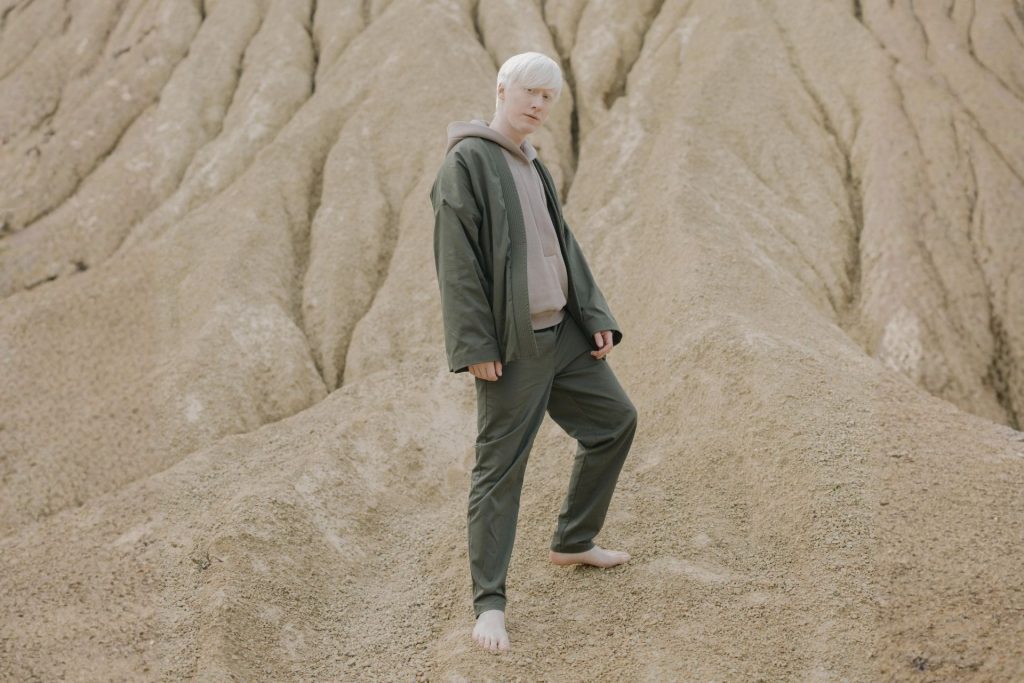 Man with albinism stands on brown sand slope