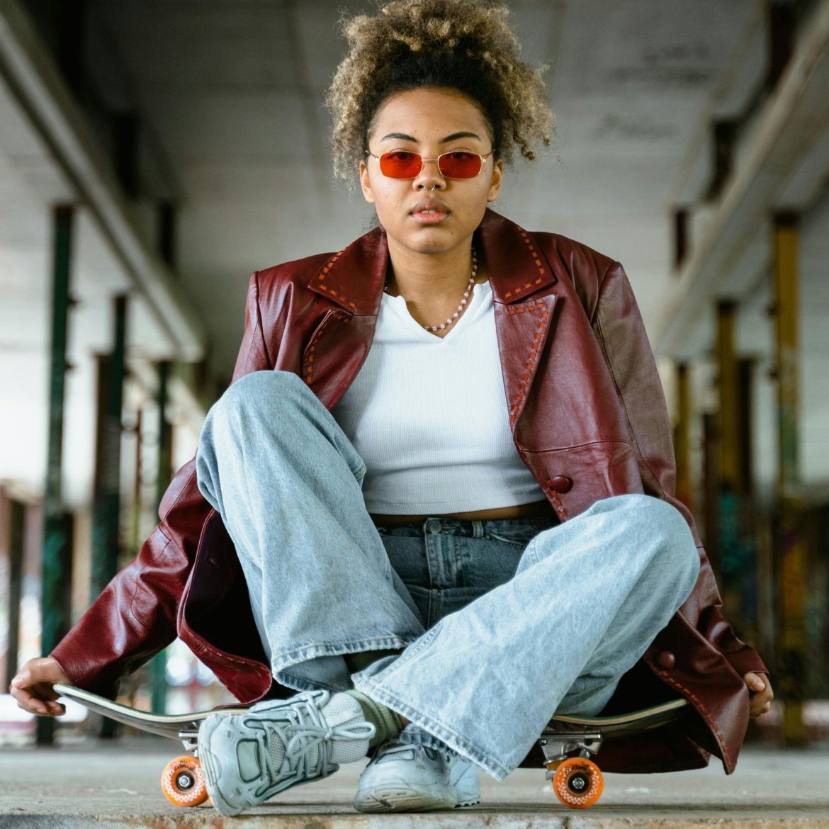 Woman wearing red sunglasses sits on top of a skateboard