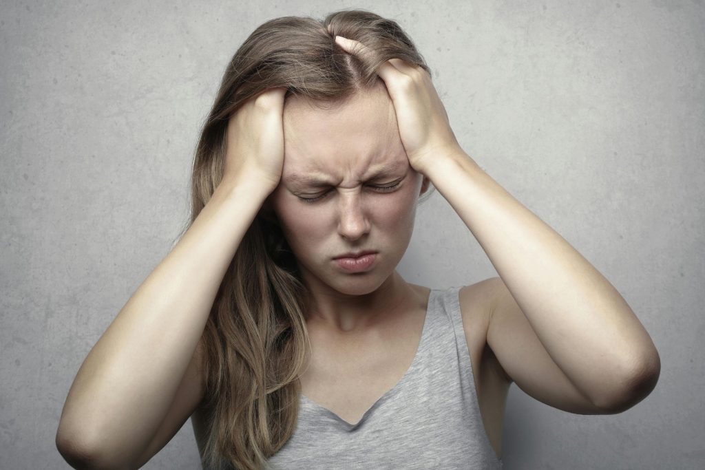 Woman clasps her hands over her temples and closes her eyes