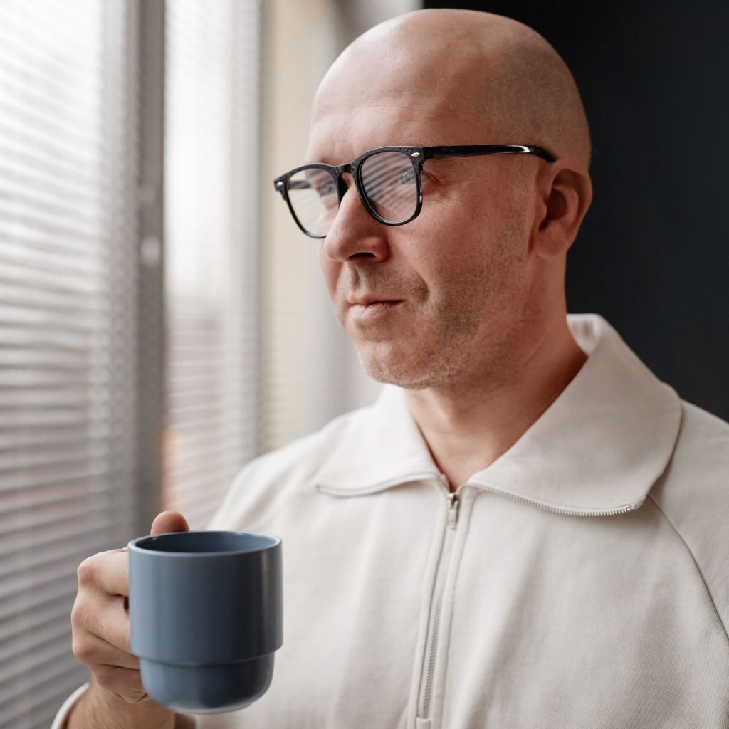 Bald man wearing round glasses and holding a mug