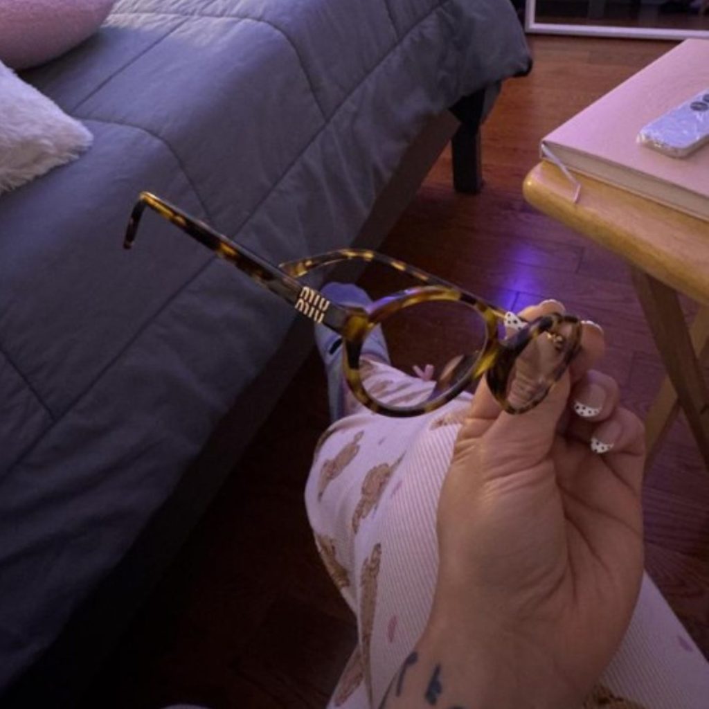 Woman holds a pair of brown oval Miu Miu MU 01XV glasses