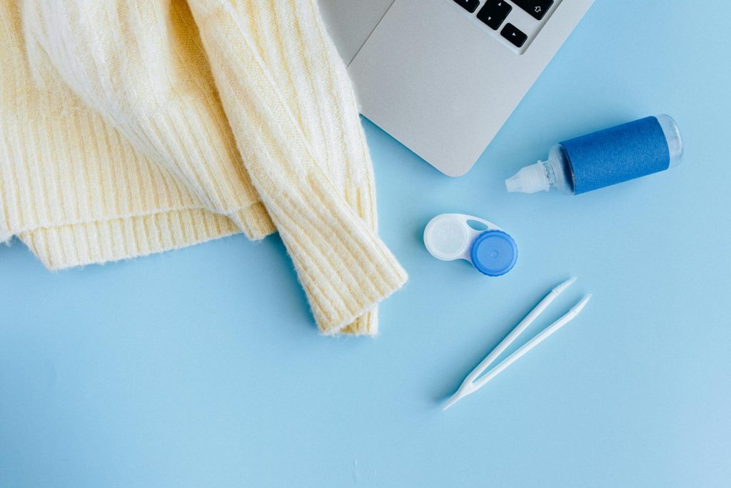 Contact lens, solution, sweater, and laptop against a blue background