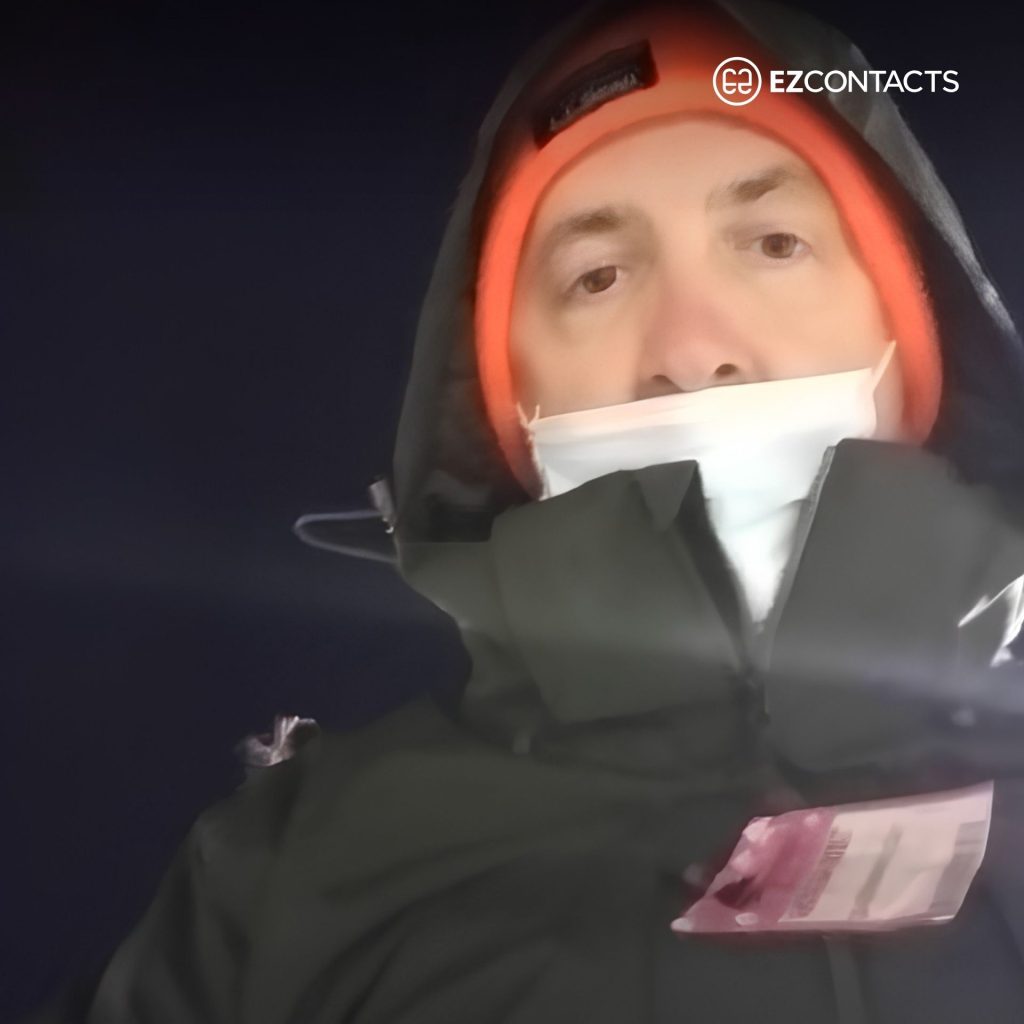 Man in a black jacket, orange beanie, and face mask